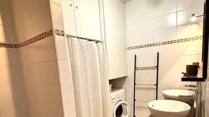 Un baño pequeño con lavadora, dos lavamanos y cortina de ducha.
