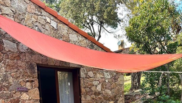 Un edificio de piedra con un patio empedrado, una mesa redonda con sillas y un toldo rojo.