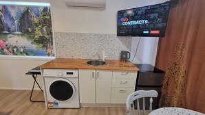 A compact kitchen with a washing machine, a sink, and a television mounted on the wall displaying a program. - Mountain Creek Retreat (Mountain Creek)