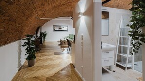 Un corridoio con pavimento a spina di pesce, parete in mattoni e una porta bianca che conduce a un bagno con lavandino bianco e una pianta.