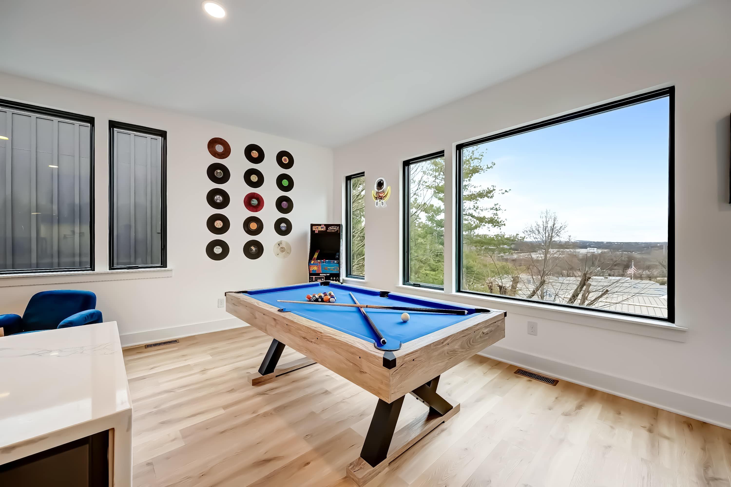 A pool table in a room with large windows, a wall of vinyl records, and a blue chair.