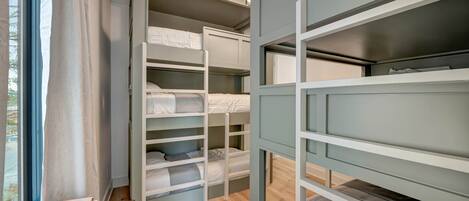 A room with bunk beds, a window with curtains, and a small table with a lamp.