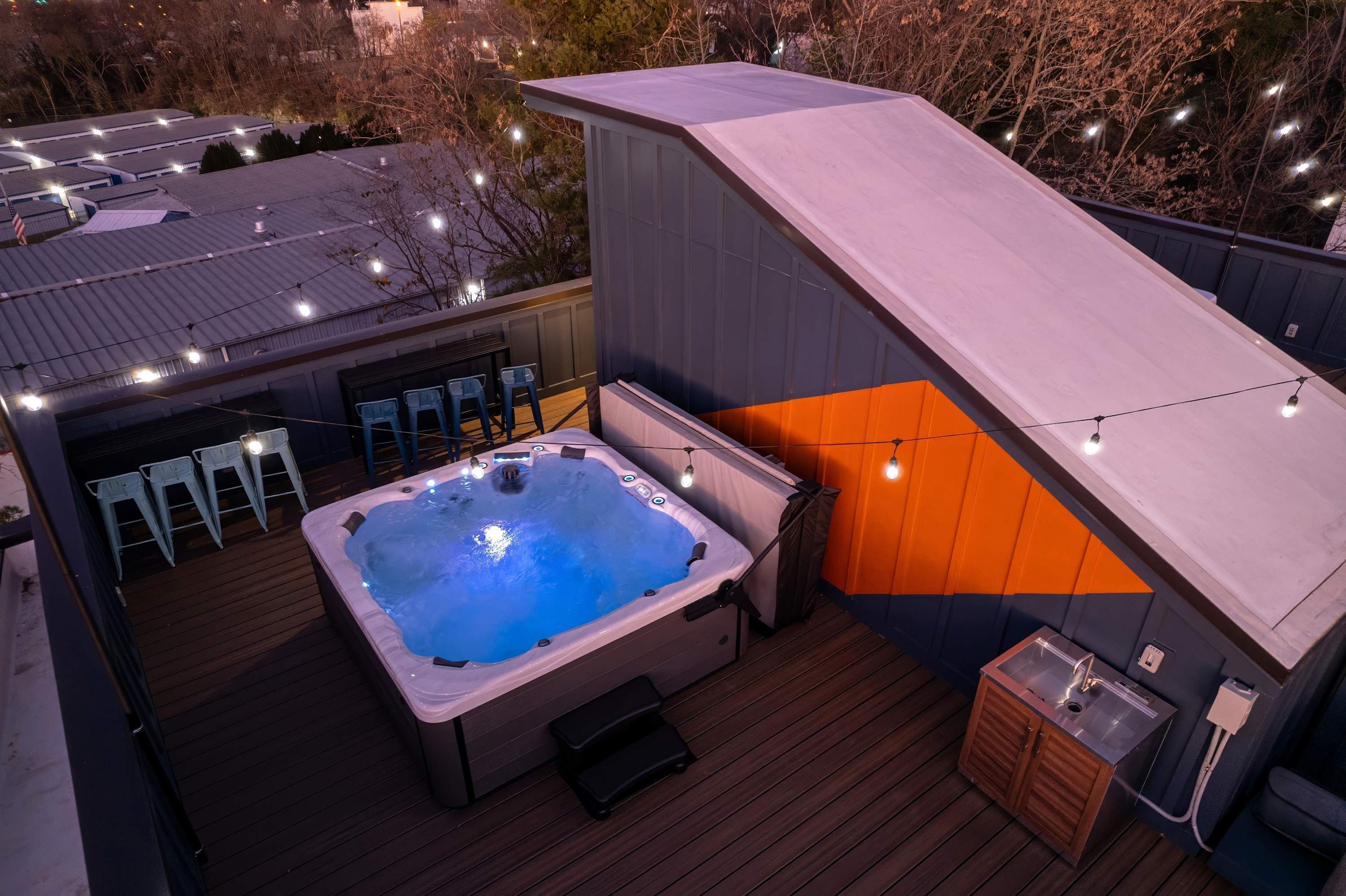 Un bain à remous sur une terrasse en bois, avec une chaise longue et un petit lavabo.