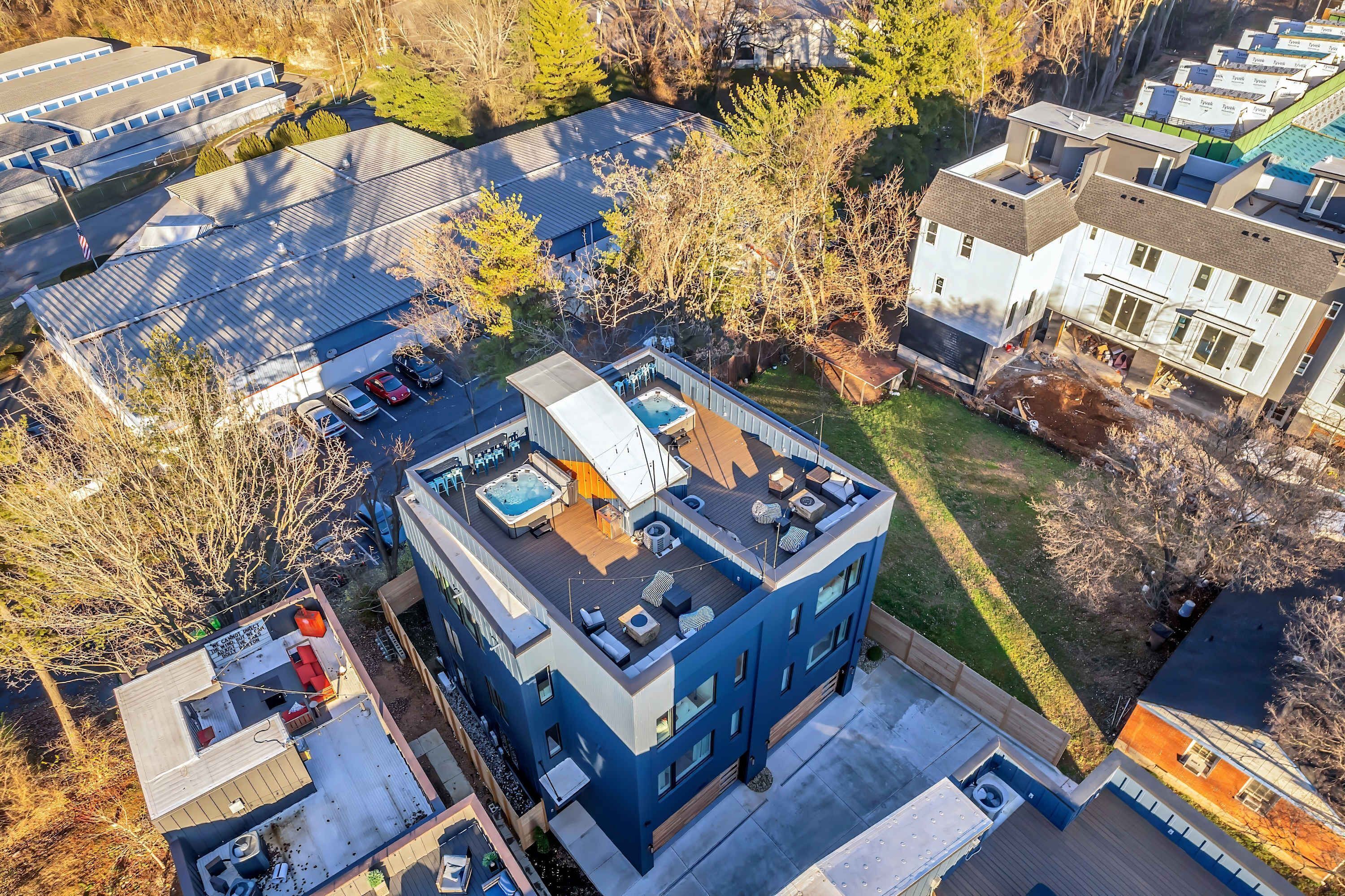 A modern multi-story building with a rooftop deck featuring outdoor seating and a hot tub.