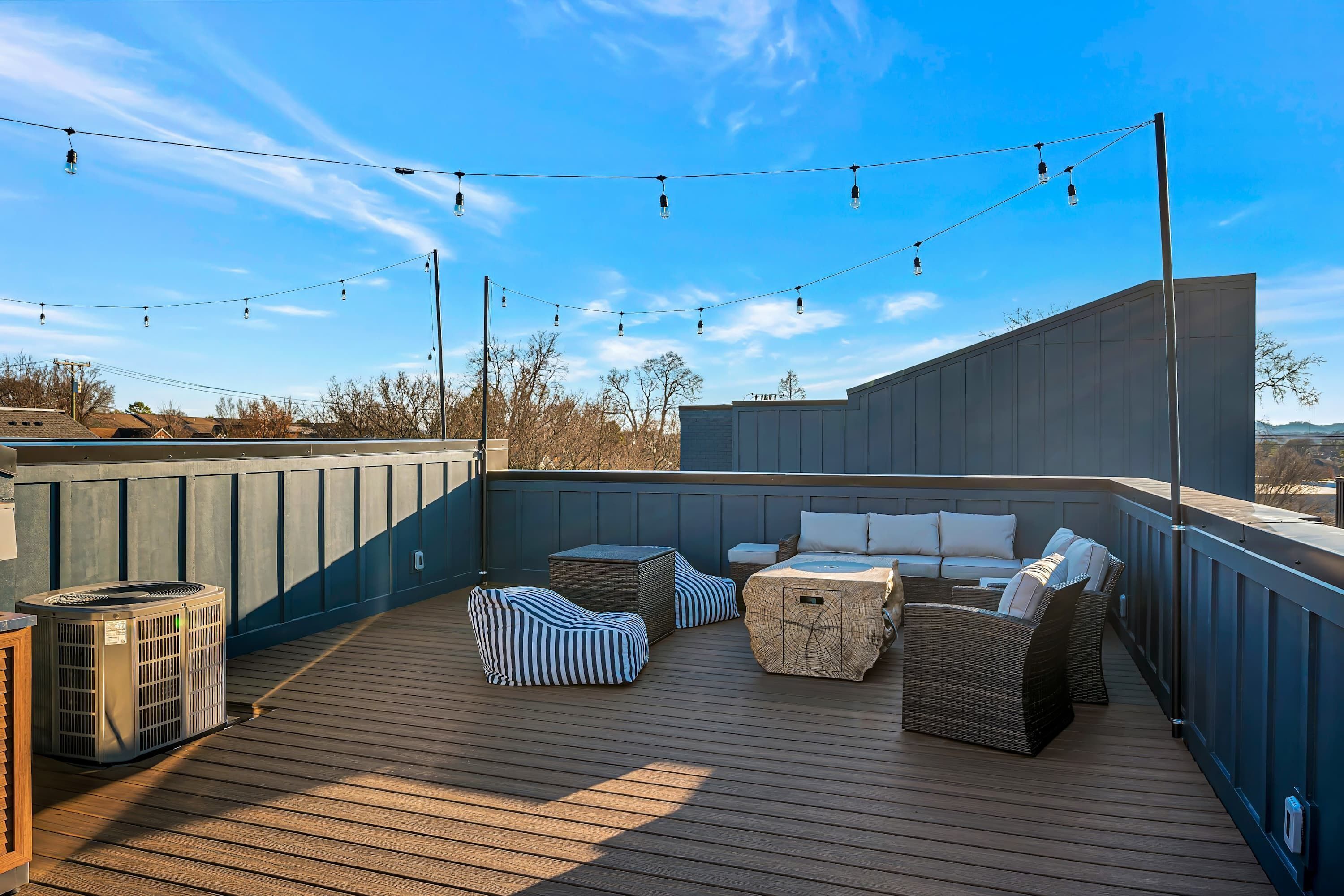 A rooftop deck with outdoor furniture, string lights, and a view of the surrounding landscape.