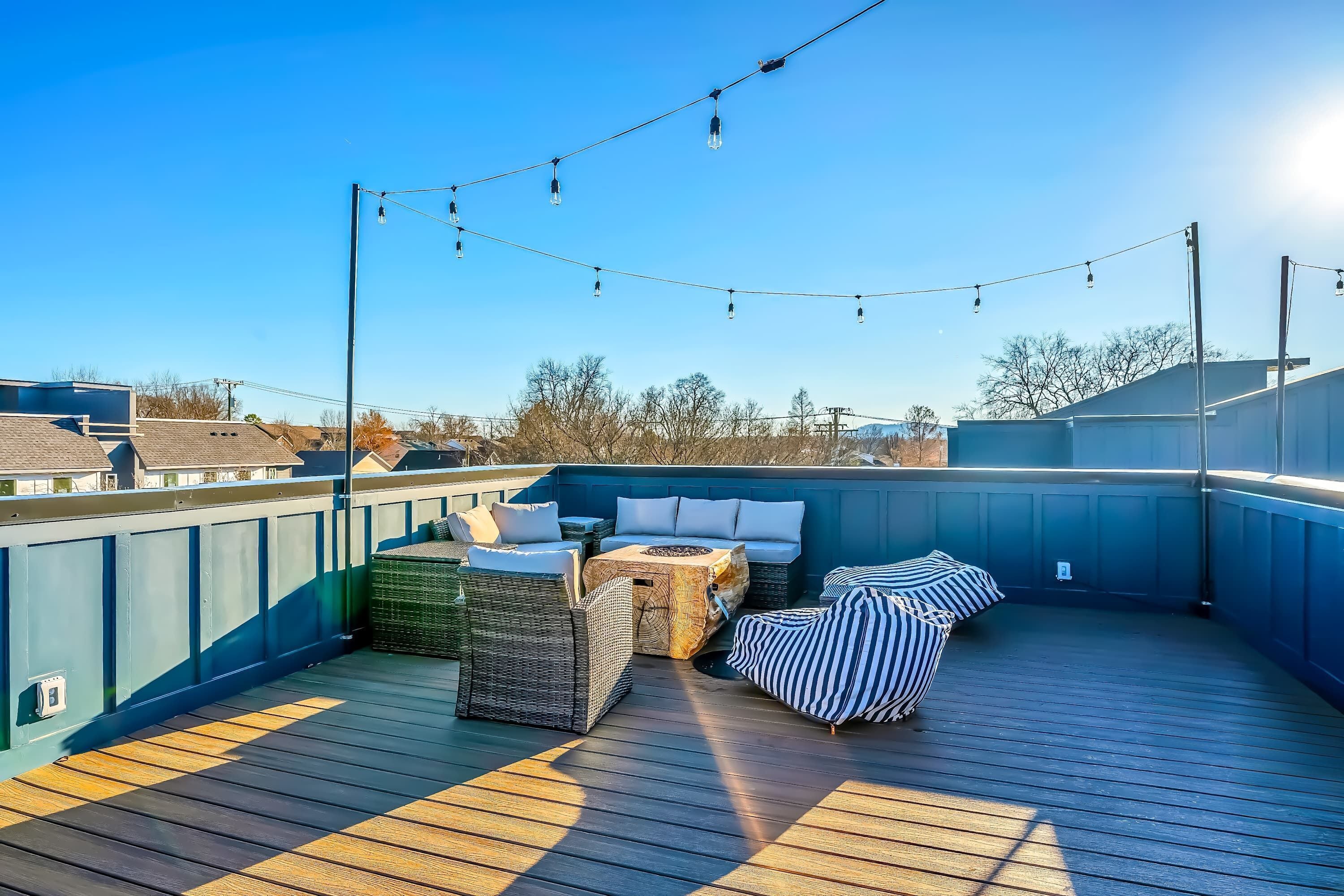 Une terrasse sur le toit, aménagée avec du mobilier d’extérieur, des guirlandes lumineuses et un ciel d’un bleu éclatant.