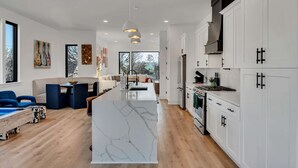 Una cocina moderna con armarios blancos, una isla central y un área de comedor con sillas azules.