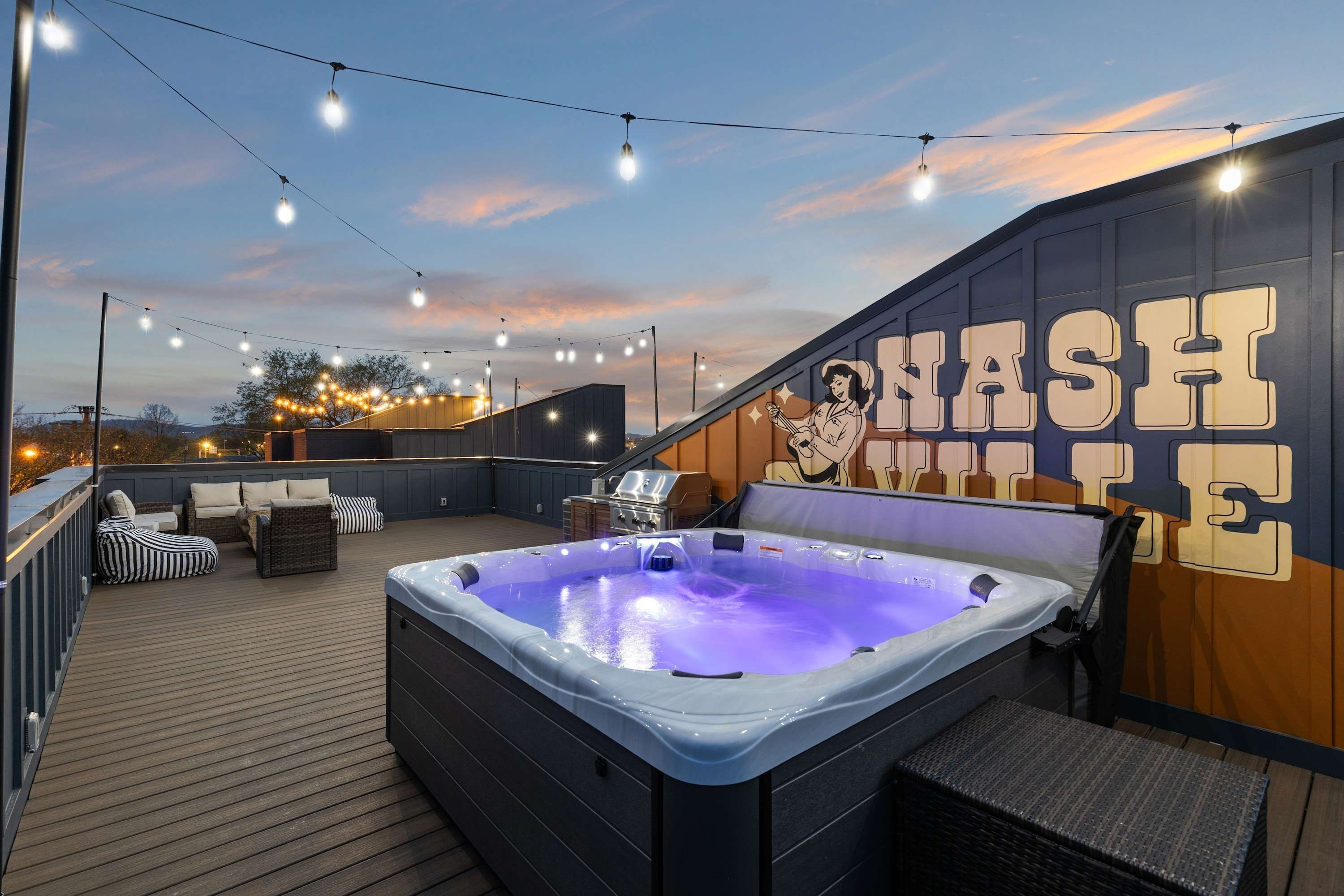 A rooftop patio with a hot tub, string lights, and a mural with the word "NASHVILLE".
