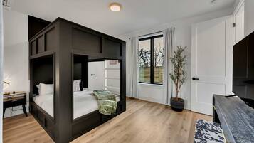 A modern bedroom with a bunk bed, a desk, a potted plant, and a TV.