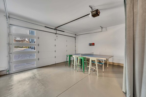 A garage with a ping pong table and stools, a ceiling-mounted projector, and a garage door with windows. - Hot Tub Game Room Rooftop Downtown Nashville (Nashville)