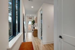 Un couloir moderne avec un banc, une porte en bois et une vue sur l’extérieur.