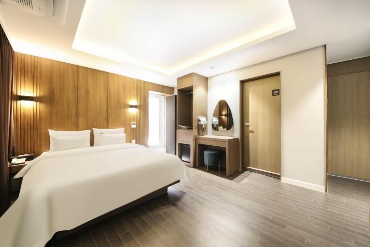 Una habitación de hotel moderna con una cama grande, un escritorio, un espejo y un armario.