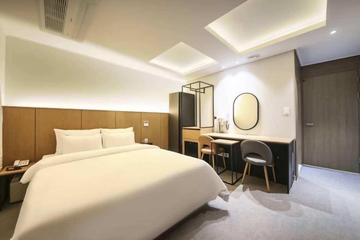 Una habitación de hotel con una cama grande, un escritorio, una silla, un espejo y un armario.