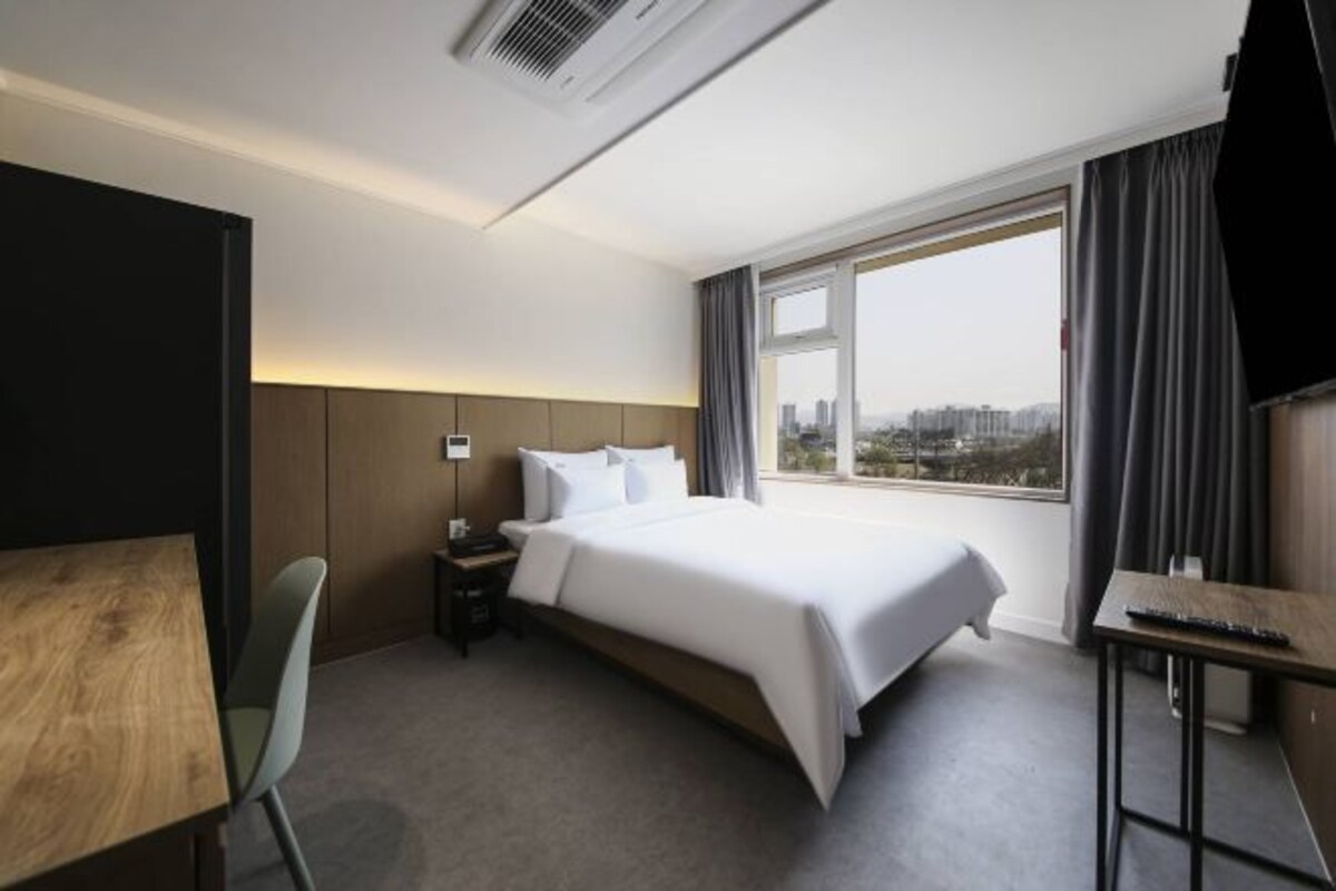 Habitación de hotel con una cama grande, un escritorio, una silla y vistas a la ciudad.
