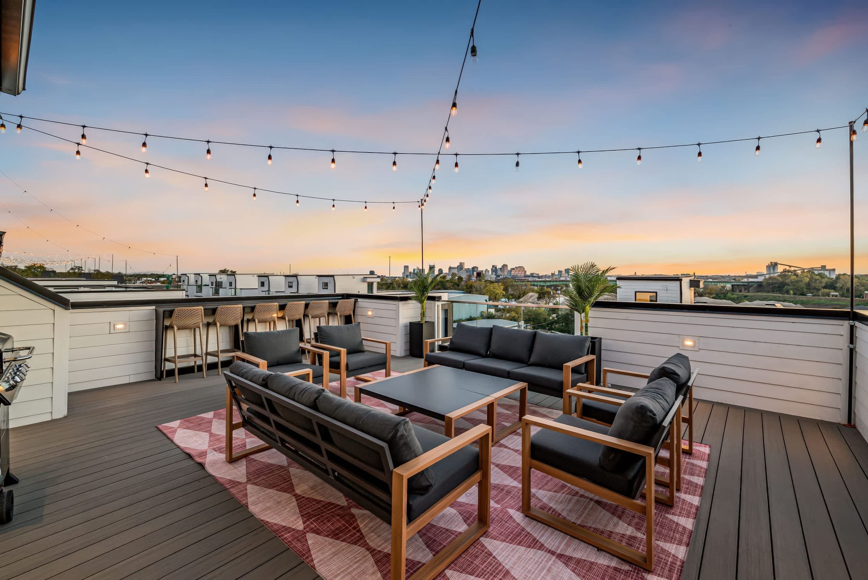Una terraza en la azotea con asientos al aire libre, luces colgantes y vistas a la ciudad al atardecer.