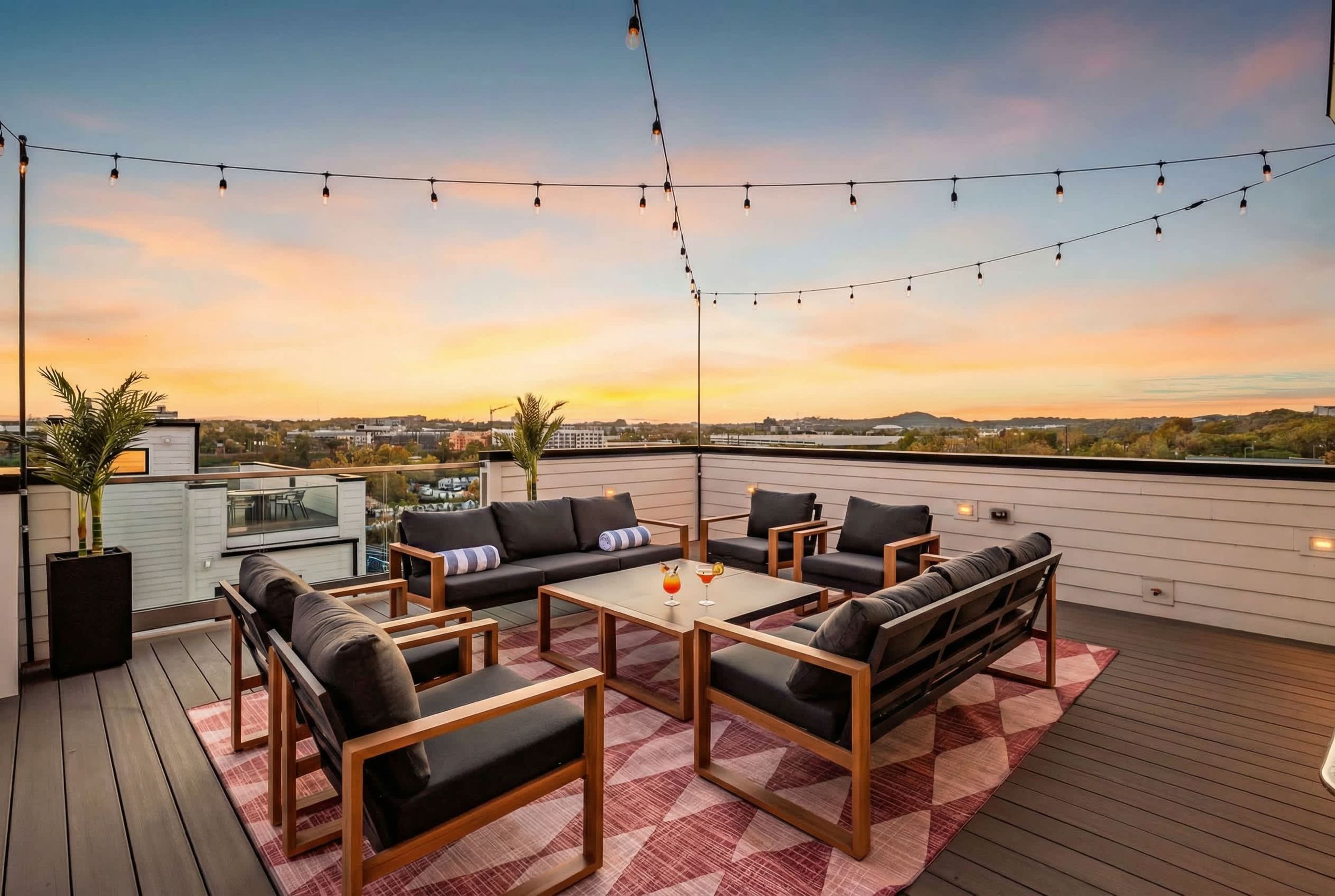 A rooftop terrace with outdoor seating, string lights, and a view of the sunset.