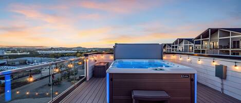 Terraza en la azotea con jacuzzi, asientos al aire libre y luces colgantes.