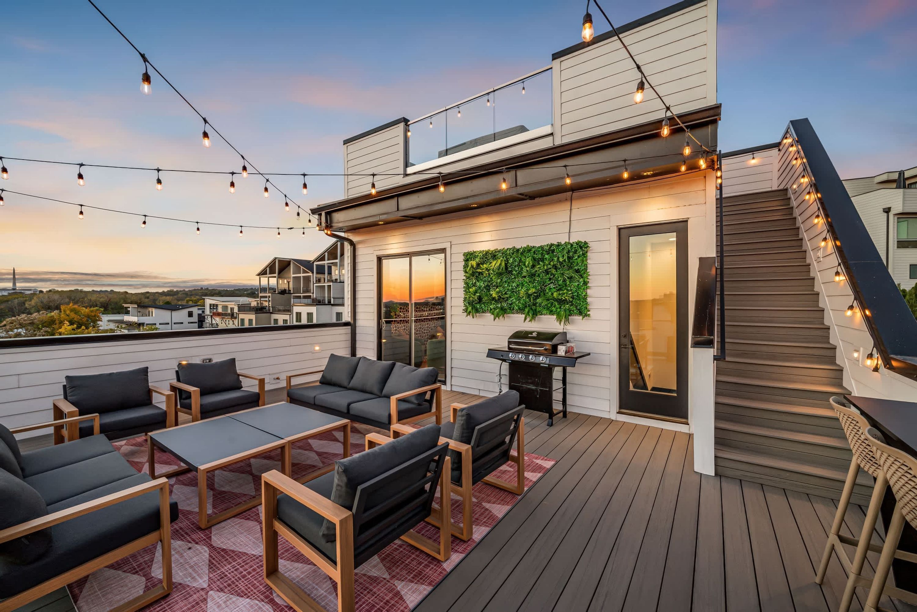 Terraza en la azotea con mobiliario exterior, una parrilla y luces colgantes.