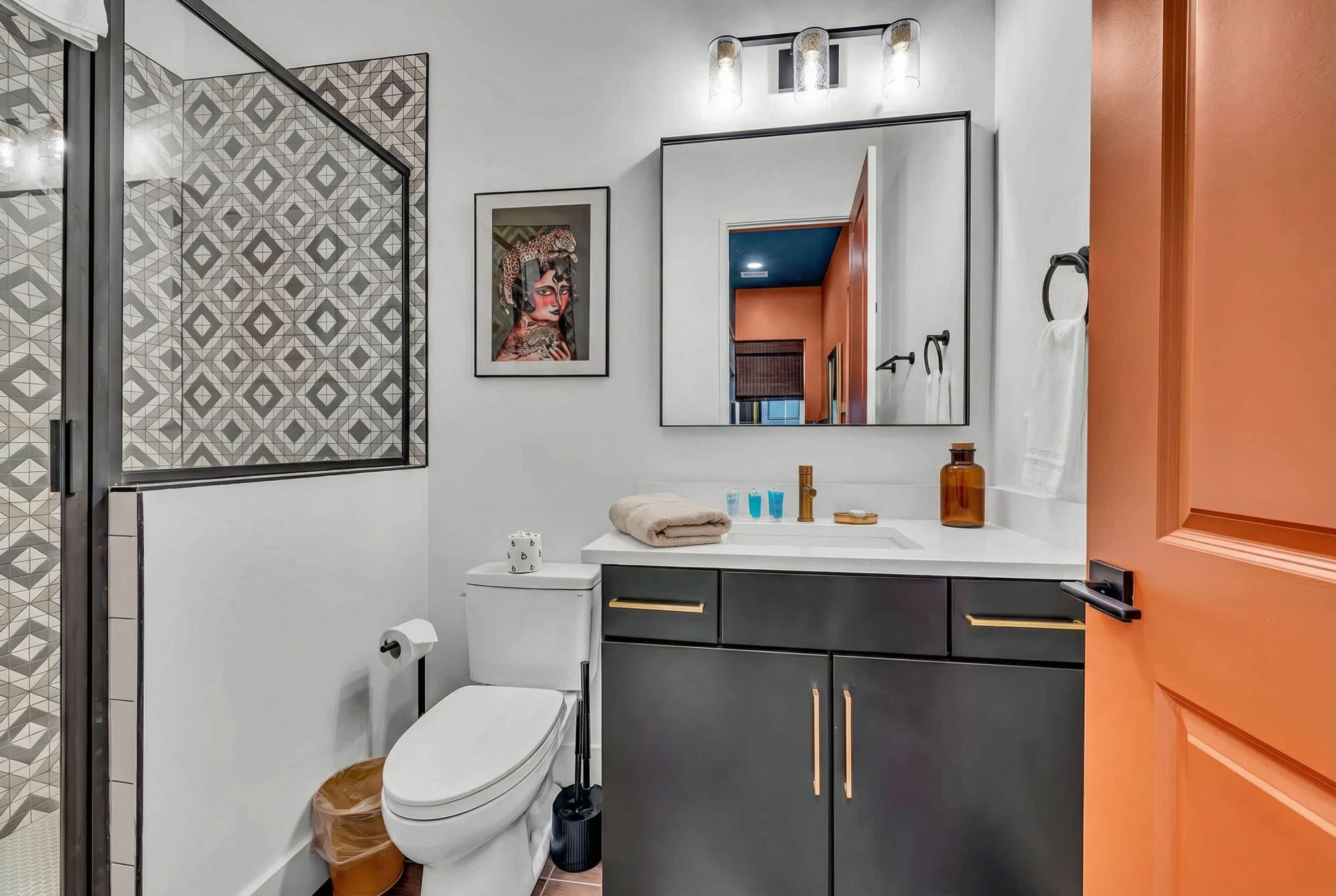 A modern bathroom with a white toilet, black cabinets, a mirror, and a patterned wall.