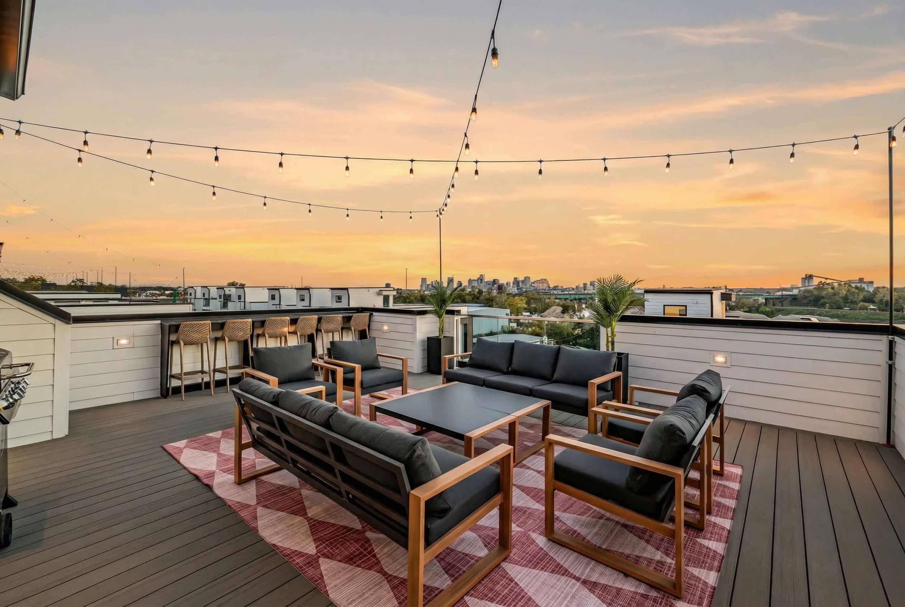 A rooftop patio with outdoor seating, string lights, and a city view at sunset.