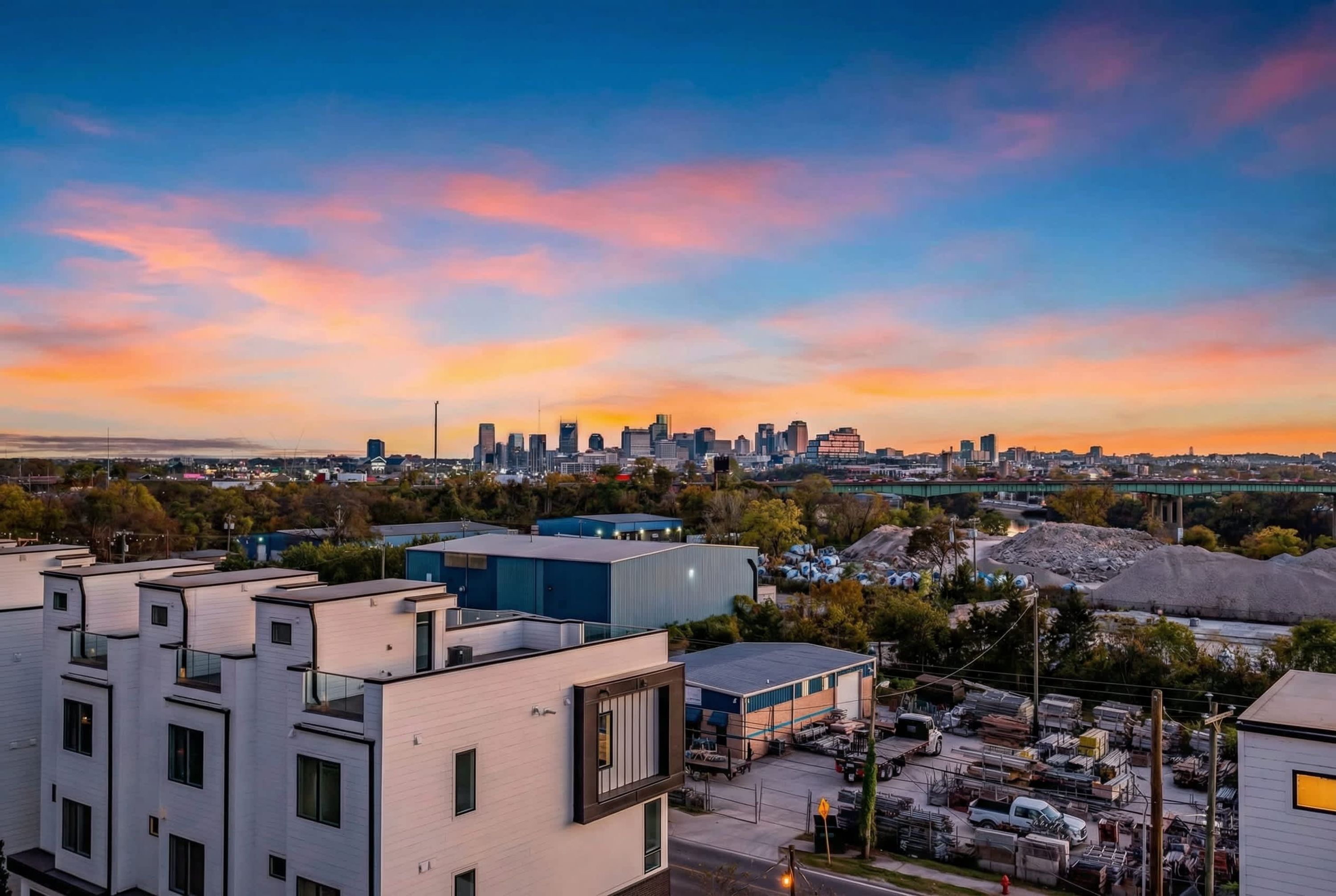 A city skyline at sunset with modern buildings and a river.
