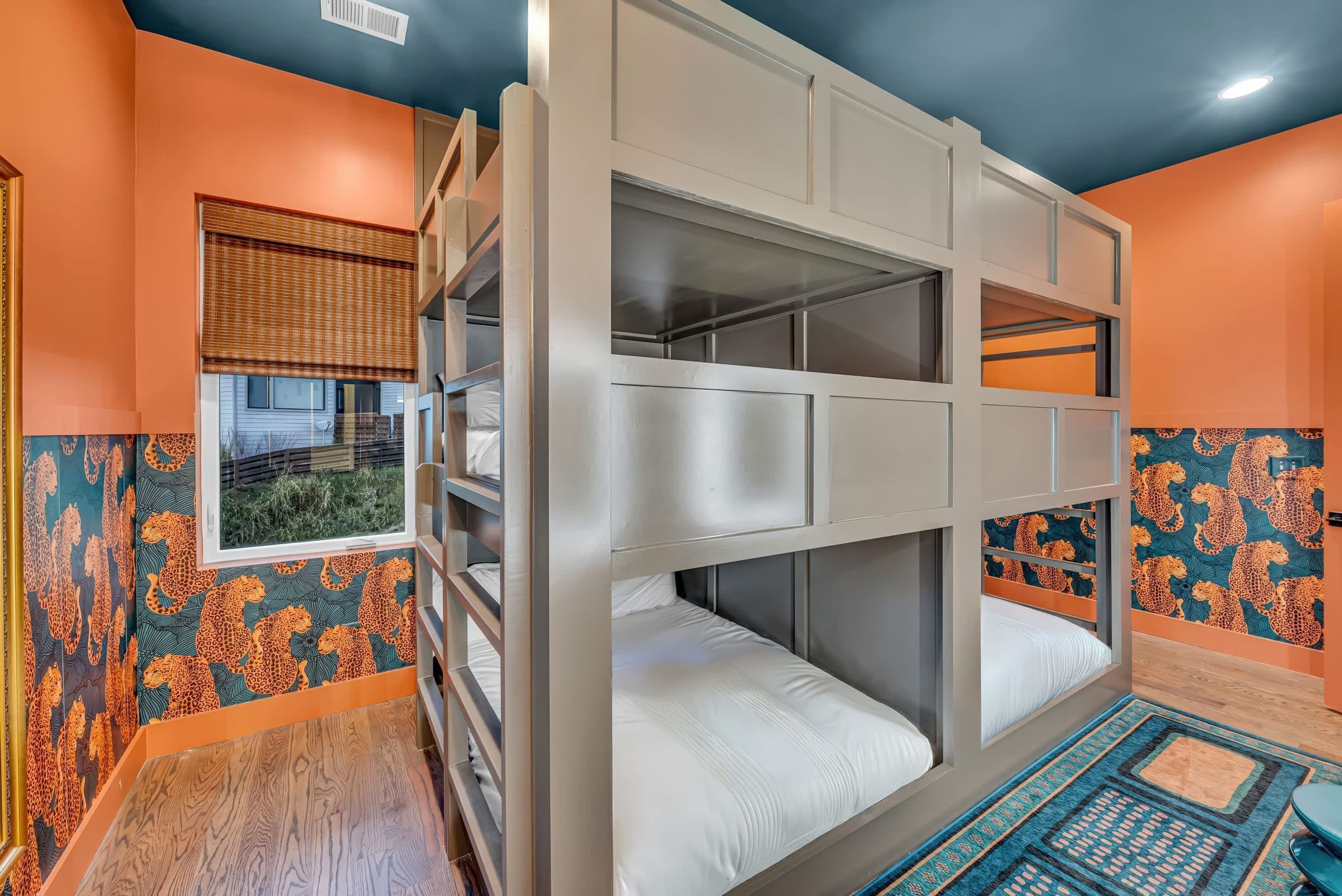 A bunk bed room with orange walls, patterned wallpaper, and a window with blinds.