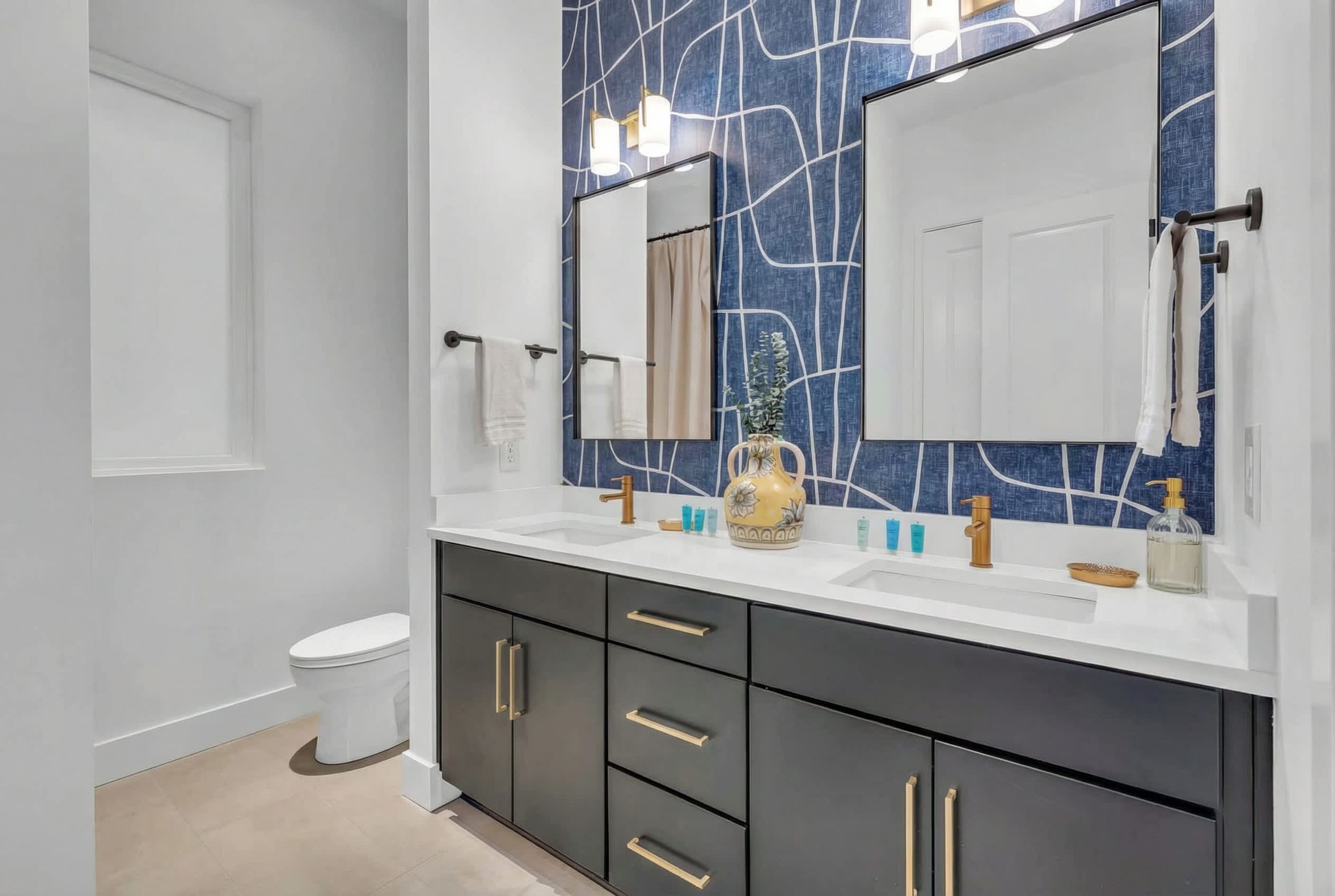 A modern bathroom with a white sink, dark cabinets, and a blue patterned wall.