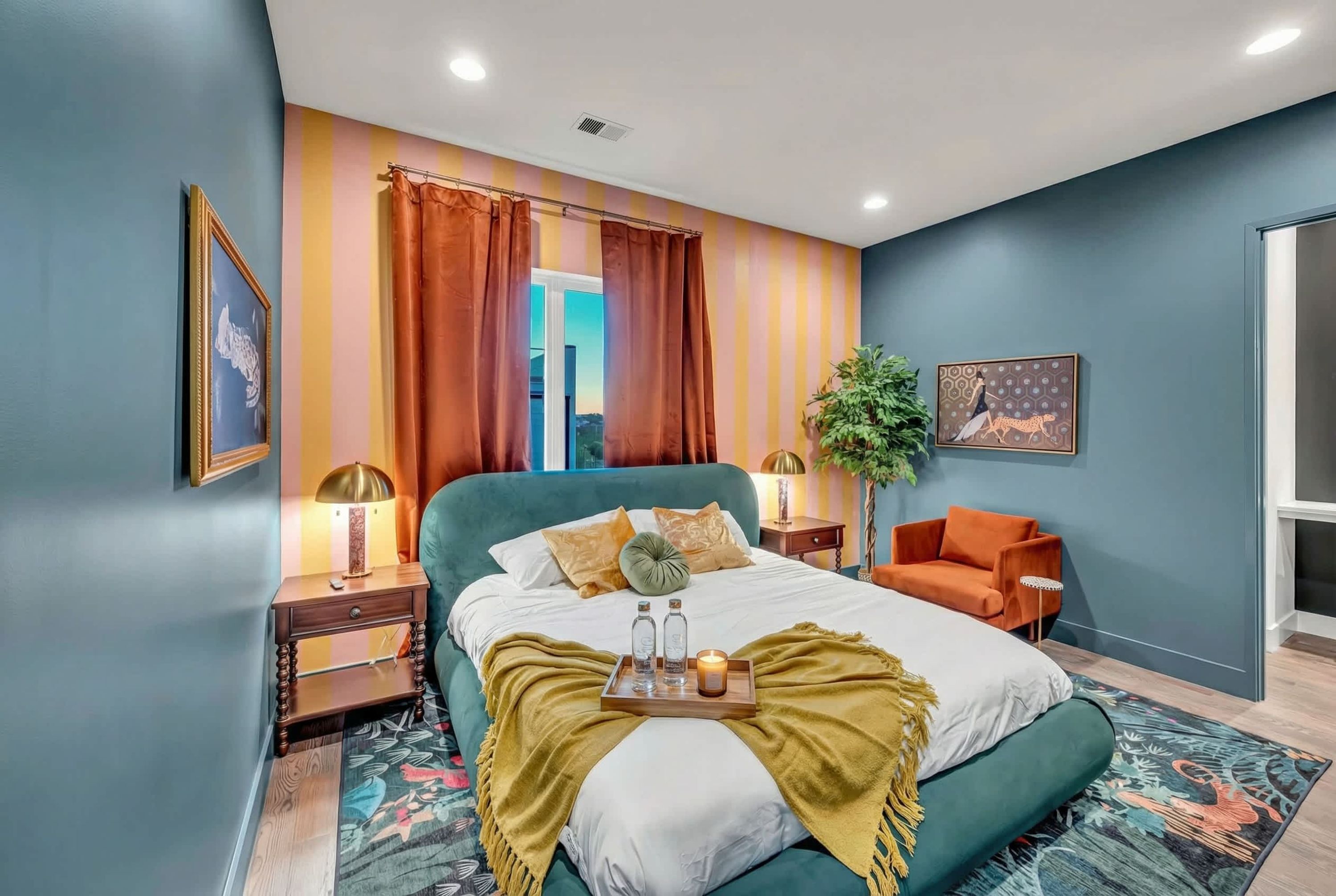 Una camera da letto con un letto verde, un comodino in legno, un tavolino, una pianta in vaso e un quadro appeso al muro.