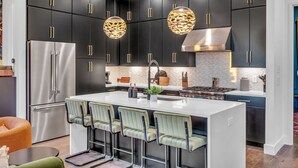 A modern kitchen with dark cabinetry, stainless steel appliances, and a central island with bar stools. - Disco Lounge Double Rooftop Hot Tub Nashville (Nashville)