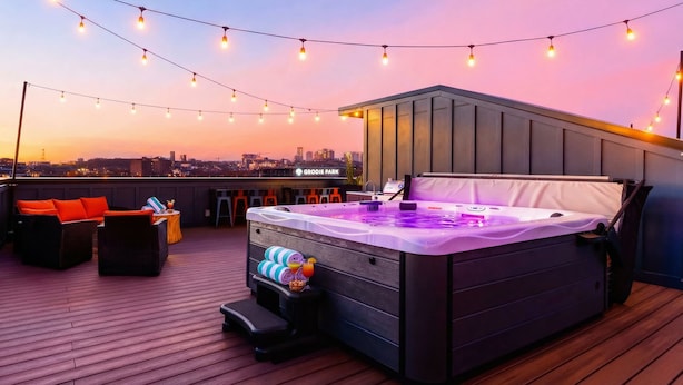 Terraço no telhado com banheira de hidromassagem, luzes de Natal e vista da cidade ao entardecer.