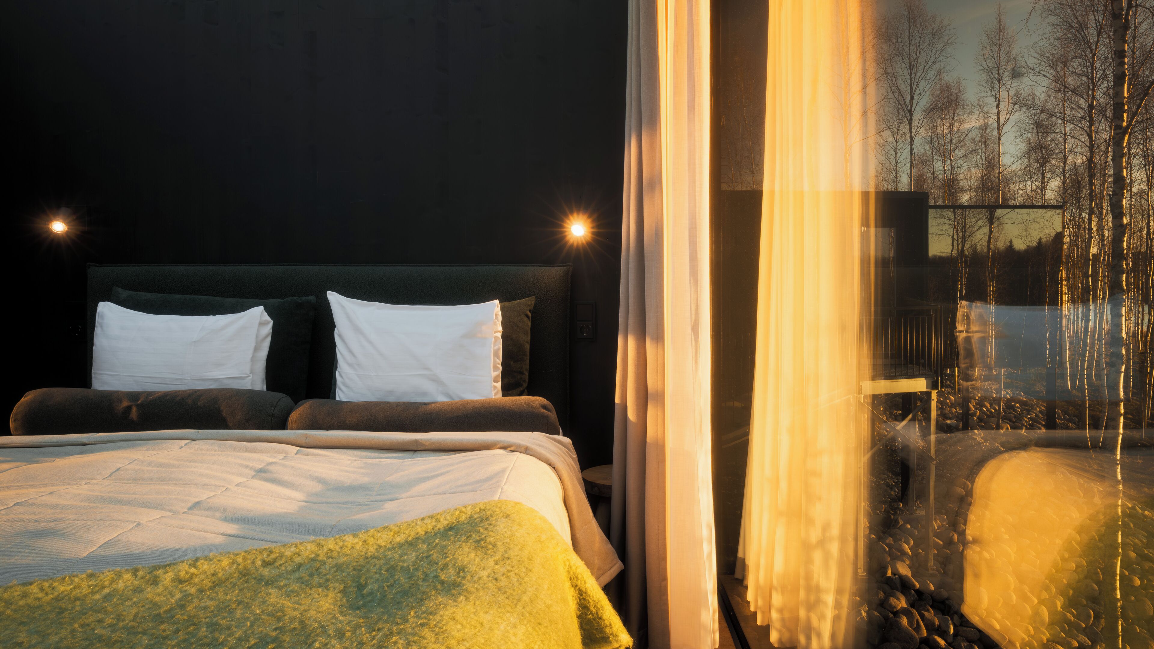 Een slaapkamer met een groot bed, twee bedlampjes en een raam met uitzicht op bomen en een gebouw.