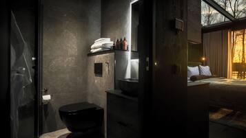 A modern bathroom with a black toilet, a sink, and a mirror. There is a towel rack with folded towels and a bottle of hand soap.