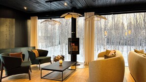 A modern living room with a fireplace, large windows, and a view of a snowy forest. - Silver Birch Resort (Rovaniemi)