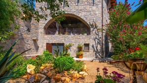 A stone building with a balcony, surrounded by a garden with various plants and flowers. - Villa Belladonna - Heraklion Private Pool Getaway (Faistos)