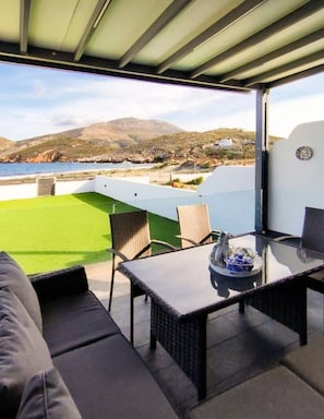 Un espace extérieur abrité, avec une table et des chaises, une pelouse verdoyante et une vue sur la mer et les collines.
