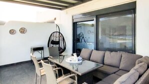 Un patio moderno al aire libre con una mesa de vidrio, mobiliario de mimbre y una zona de estar con cojines.