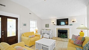 Una sala de estar con sofás amarillos, una mesa de centro blanca, una chimenea y un televisor.