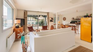 Ein modernes Wohnzimmer mit einer Couch, einem Esstisch, Stühlen und einer Küchenzeile mit einem gelben Kühlschrank.