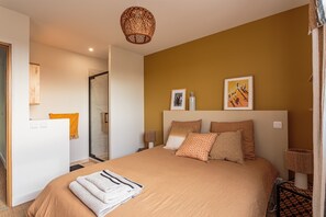 A bedroom with a large bed, a bedside table with a lamp, and a door leading to a bathroom. - Amaya - A 10min de la Plage (Anglet)