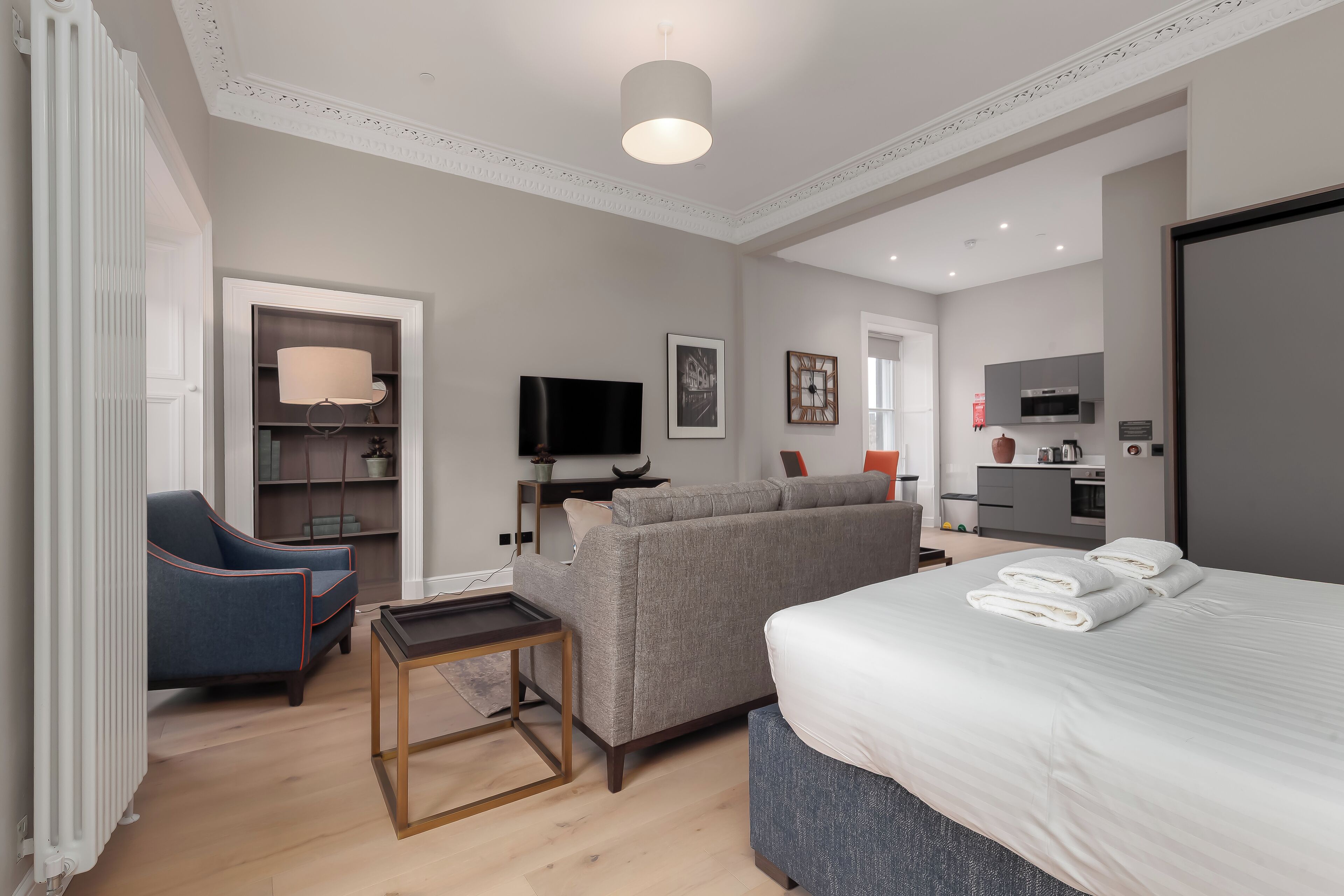 Una habitación de hotel moderna con sofá, cama con toallas, televisión, una mesita y una estantería.