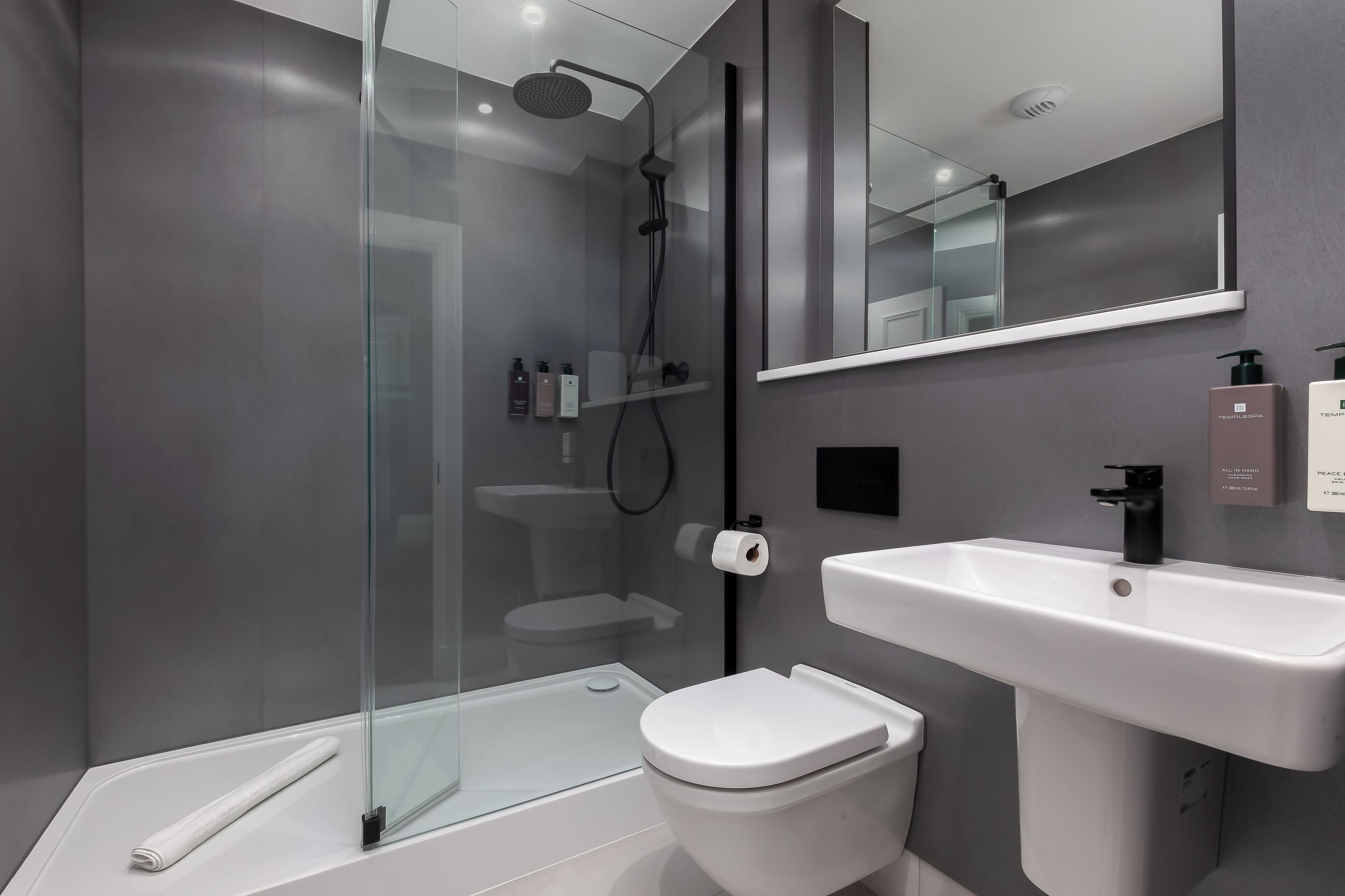 A modern bathroom with a glass-enclosed shower, a white sink, and a toilet.