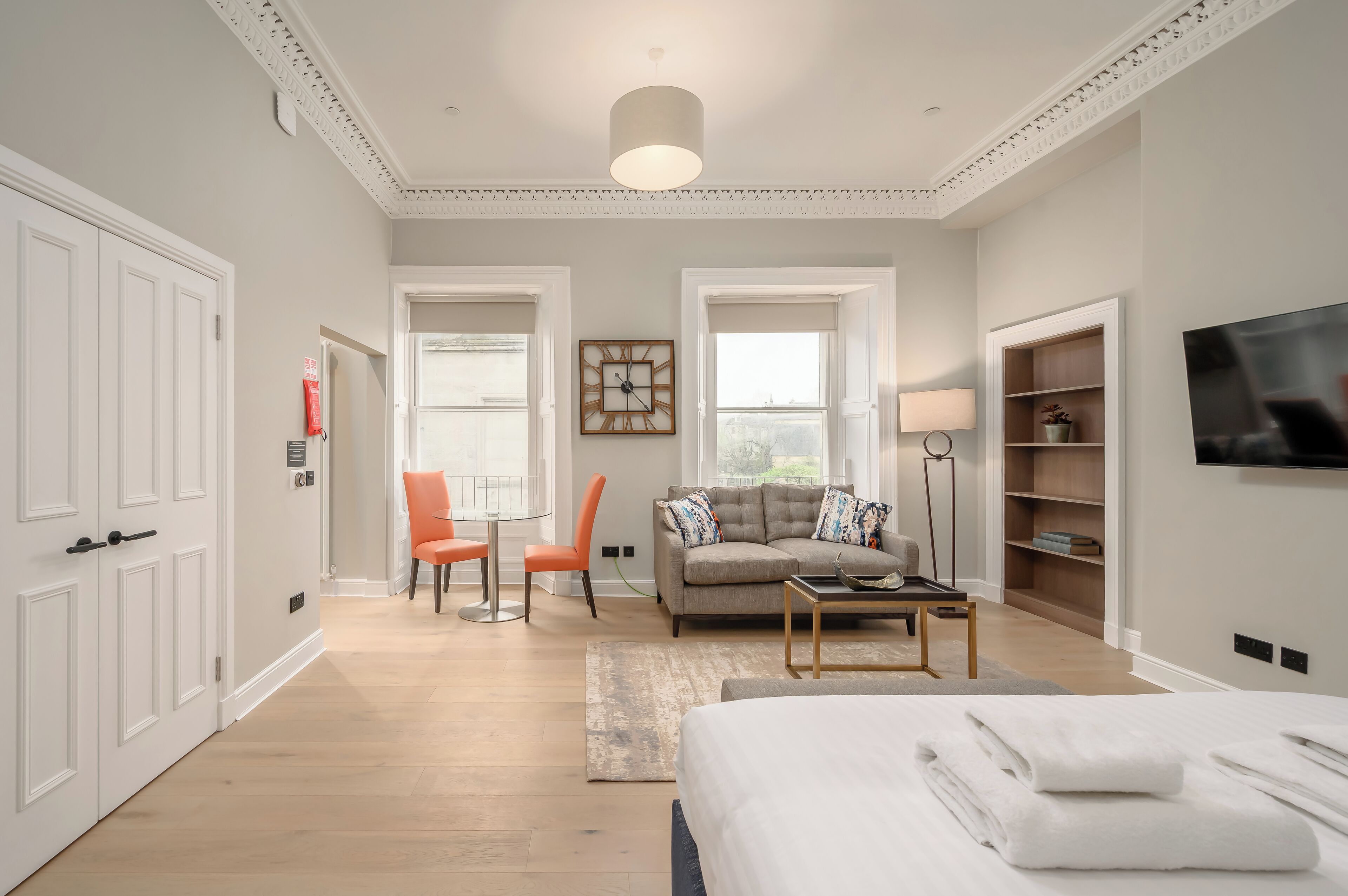 Una habitación de hotel moderna con una cama grande, un sofá, dos sillones, una mesita de centro, un televisor y una estantería.