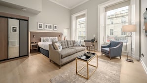 Een moderne woonkamer met een bank, salontafel en fauteuil. Er is een groot raam met uitzicht op gebouwen.