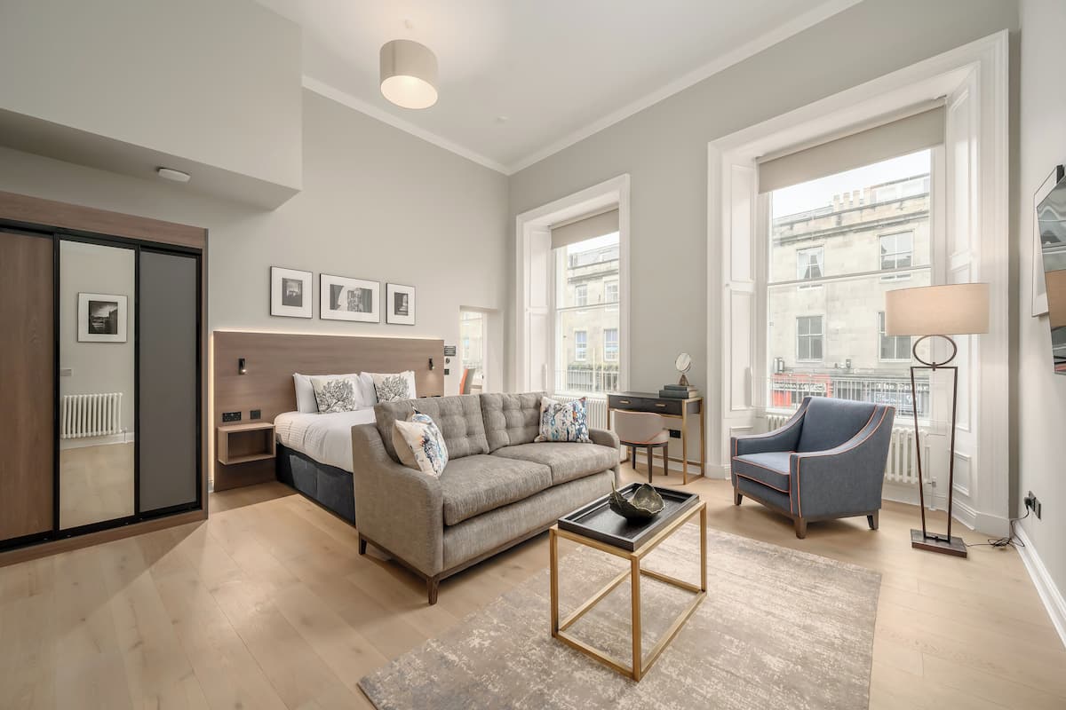 Un salon moderne avec un canapé, une table basse et un fauteuil. Une grande fenêtre offre une vue sur les bâtiments.