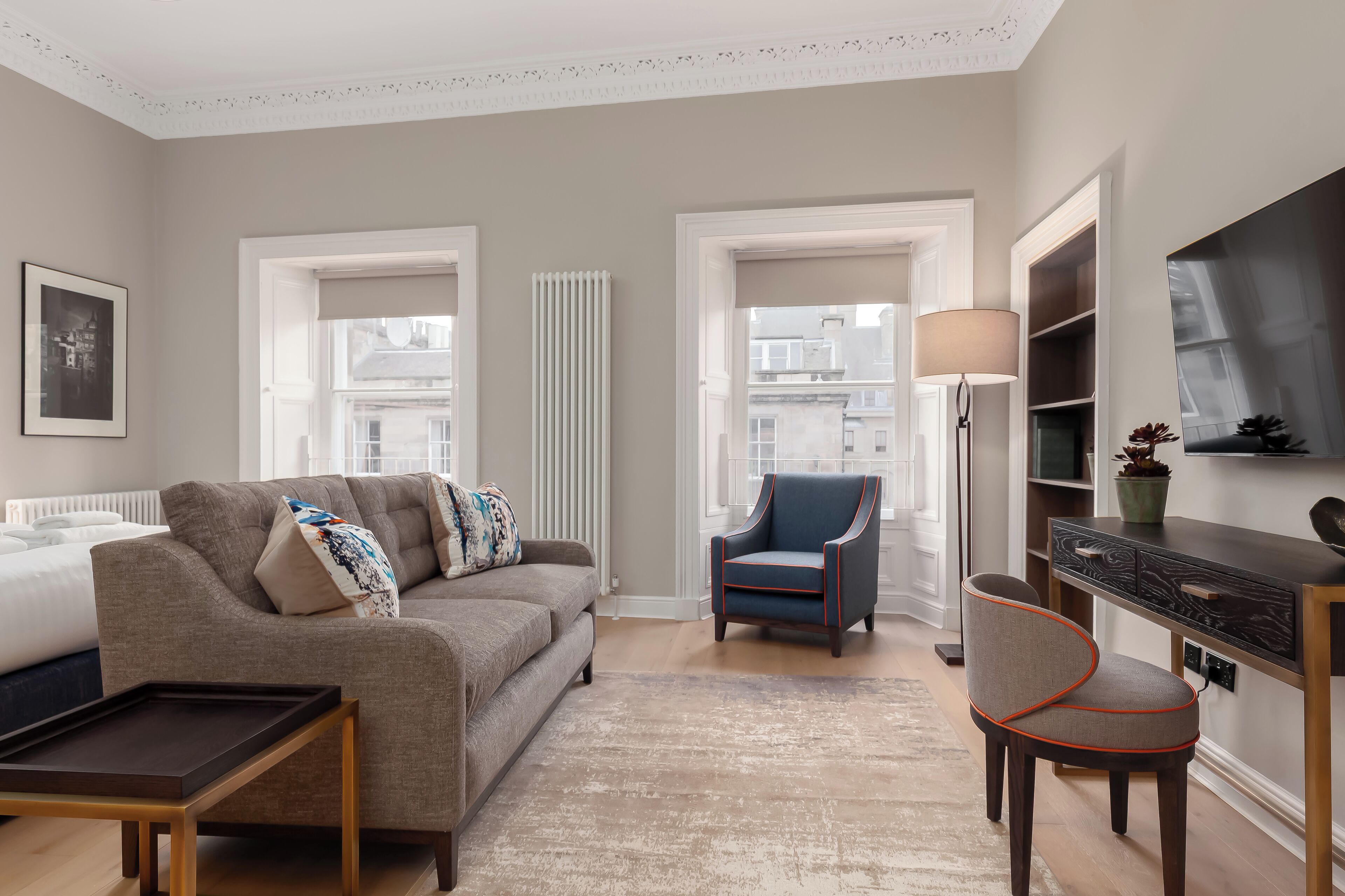A modern living room with a grey sofa, a blue armchair, a wooden coffee table, and a TV on a wooden stand.