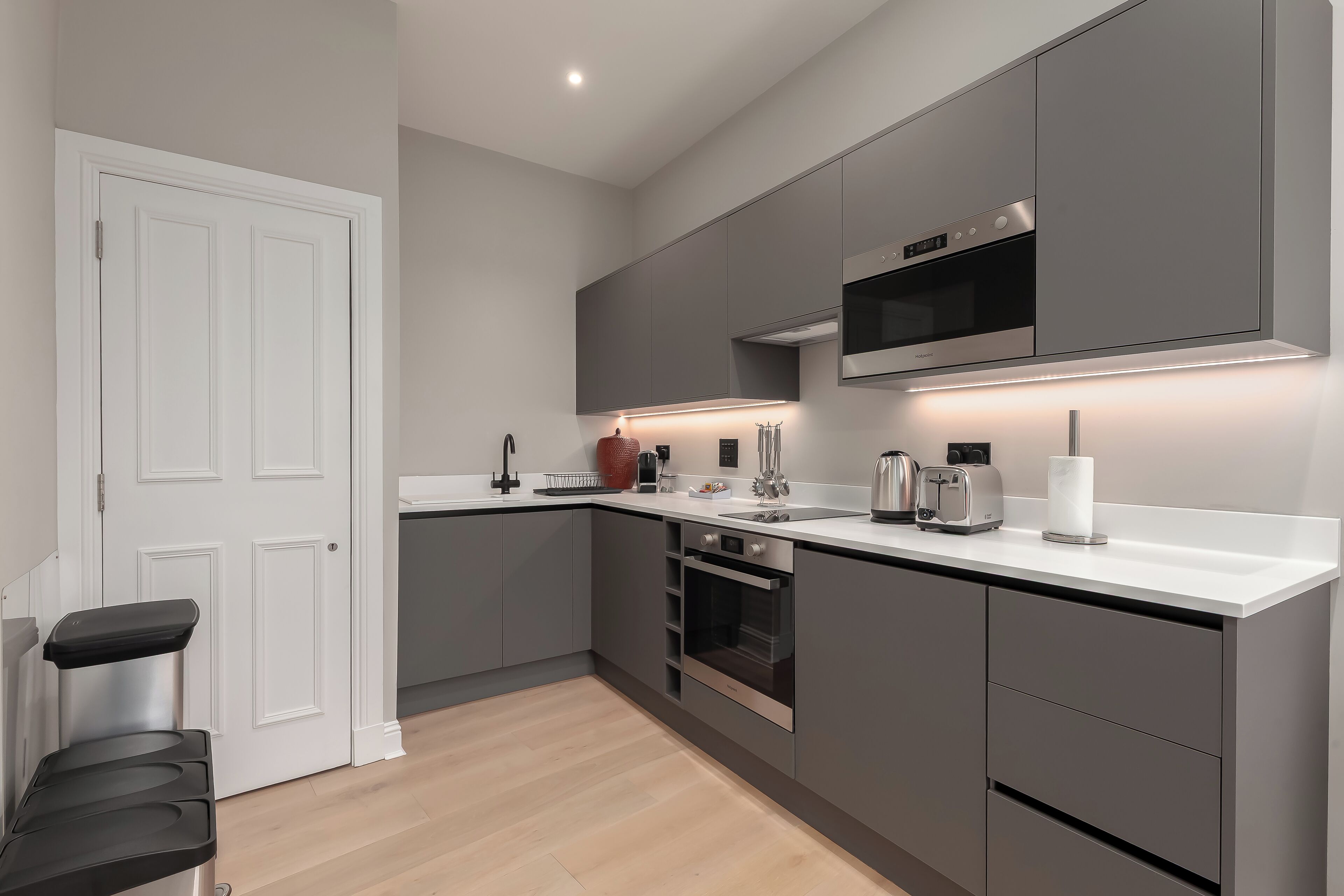 A modern kitchen with grey cabinets, a white countertop, a built-in oven, and a microwave.