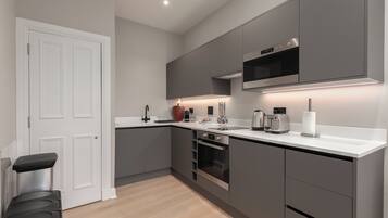 A modern kitchen with grey cabinets, a white countertop, a built-in oven, and a microwave.