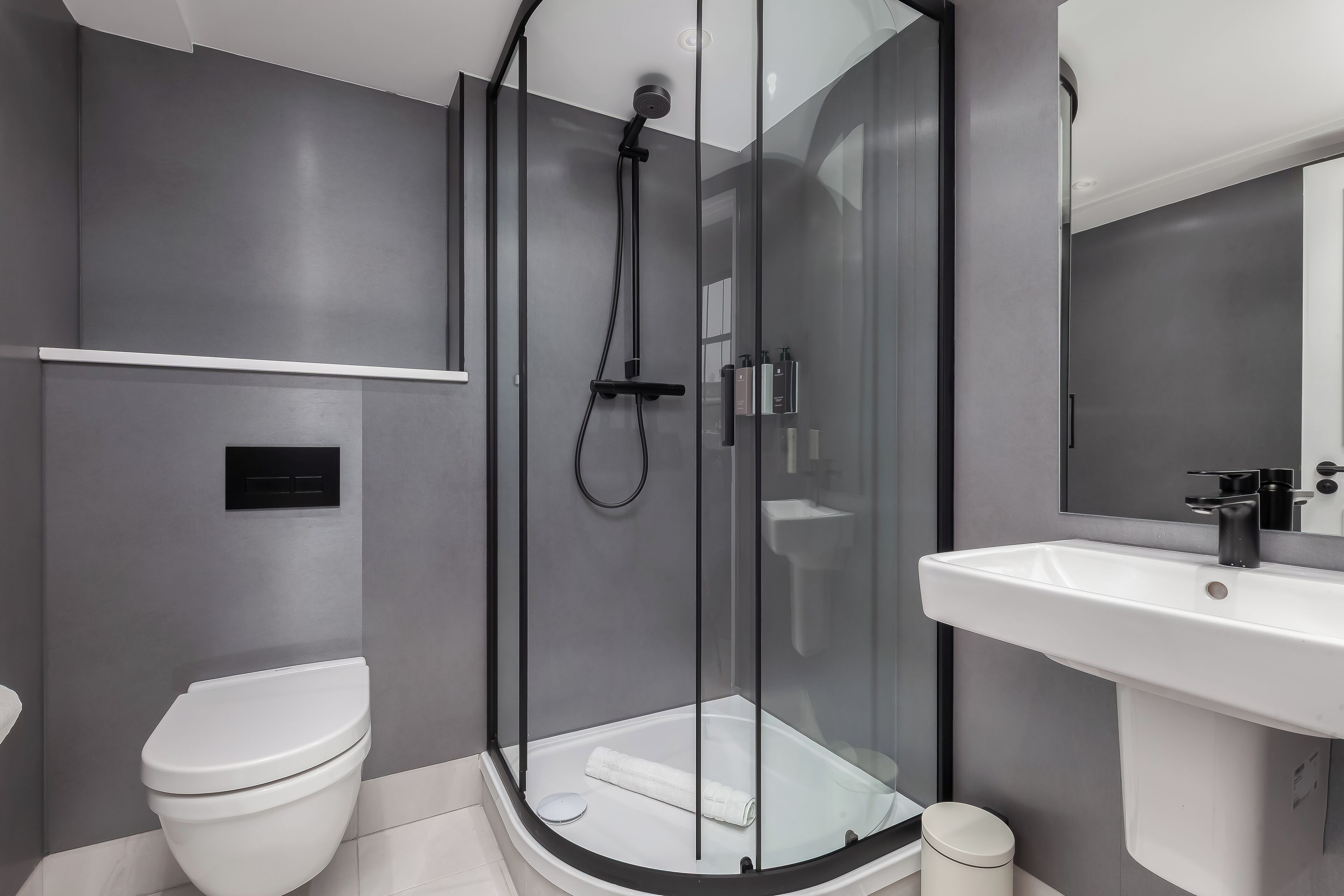 Une salle de bain moderne avec une douche à parois de verre, des toilettes blanches et un grand lavabo.