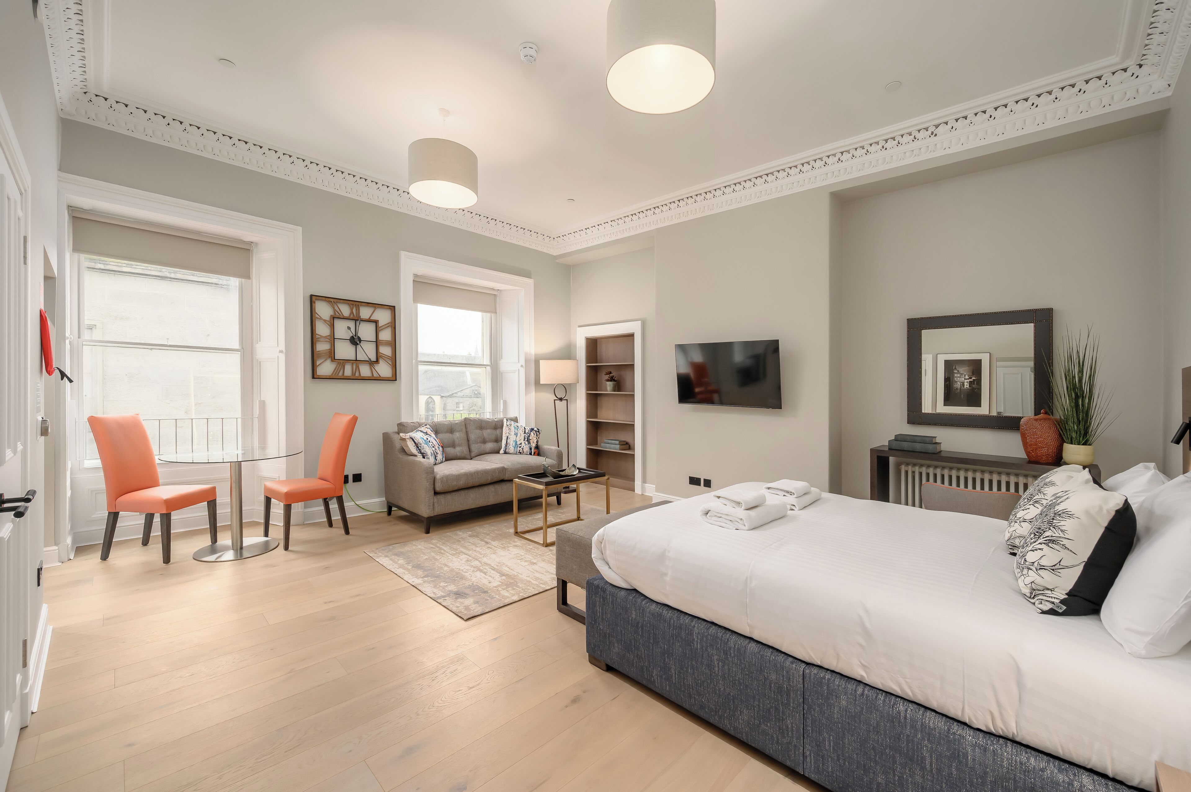 A modern bedroom with a large bed, a sofa, two chairs, a small table, a TV, and a bookshelf.