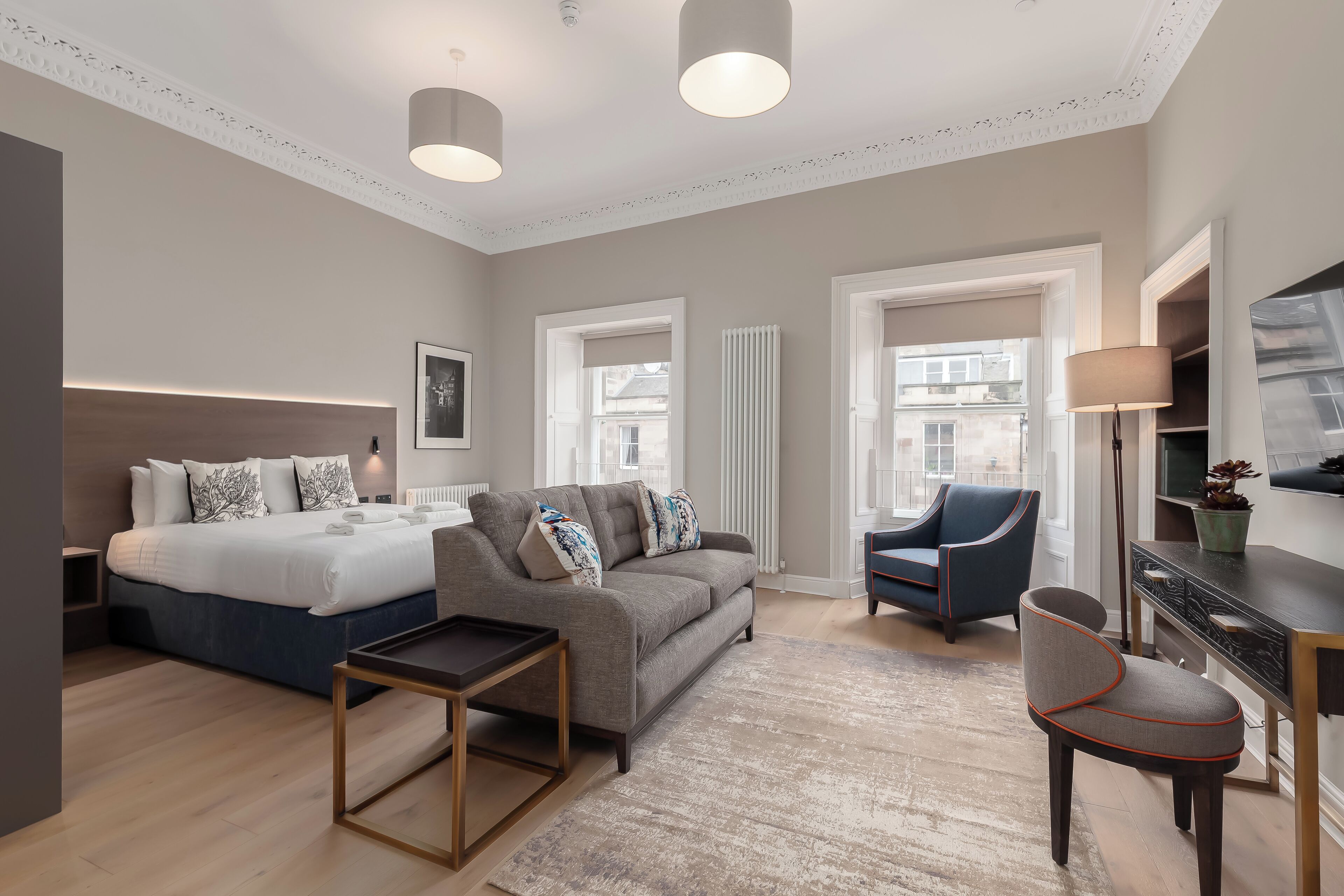 Quarto de hotel moderno com cama, sofá, poltrona e uma pequena mesa.